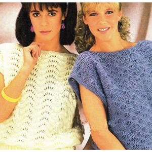 May include: Two women wearing knitted tops with openwork patterns. The woman on the left is wearing a white top and the woman on the right is wearing a light purple top.