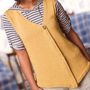 May include: Mustard yellow knitted vest with a single button closure. The vest has a V-neck and a slightly asymmetrical design. The model is wearing a striped shirt underneath. The vest is a warm, casual garment.