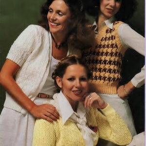 May include: Three women wearing knitted sweaters. The woman on the left is wearing a white cardigan with a delicate openwork pattern. The woman in the middle is wearing a yellow cardigan with a similar openwork pattern. The woman on the right is wearing a brown and yellow houndstooth vest over a white blouse.