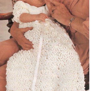 May include: A white crocheted baby gown with a satin ribbon tie. The gown has a delicate, lacy pattern and is perfect for a special occasion.