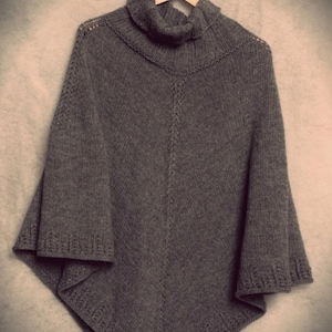 May include: A grey knitted turtleneck poncho with a cable knit pattern and a loose fit.