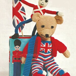 May include: A knitted teddy bear wearing a red and white striped outfit with a blue scarf. The bear is sitting next to a tin can with a picture of a toy soldier on it. A toy soldier with a red uniform and a black hat is standing on top of the bear.