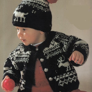 May include: A black and white knitted cardigan with reindeer designs and silver buttons. The cardigan has a white trim around the neckline and cuffs. The model is wearing a red hat with white pom-poms.
