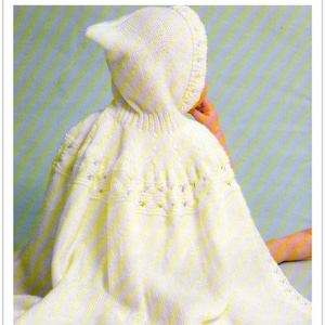 May include: A white and yellow knitted baby cape with a hood. The cape has a delicate lace pattern around the edges.