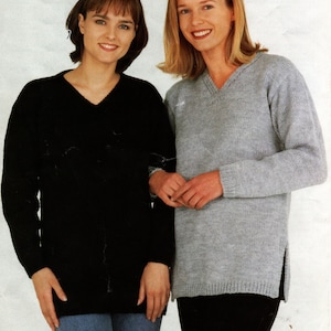 May include: Two women wearing sweaters. The woman on the left is wearing a black sweater with a V-neck. The woman on the right is wearing a light gray sweater with a V-neck and side slits.