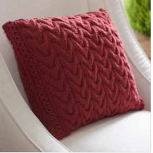 May include: A red knitted throw pillow with a cable knit pattern. The pillow is soft and plush, and would be a great addition to any living room or bedroom.