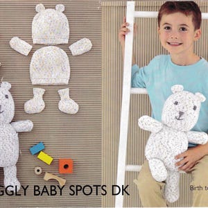 May include: A knitted teddy bear, hat, mittens, and booties set in white with speckled yarn. The image includes a child holding a teddy bear and various wooden toys. Text on the image reads "Snuggly Baby Spots DK" and "Birth to 2 years."
