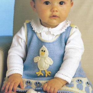 May include: A baby wearing a blue knitted dress with a white chick applique and a white lace collar. The dress has a yellow and blue trim and a row of blue chicks at the bottom.