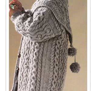 Puede incluir: Un cárdigan gris con capucha, tejido en punto de cable y con pompones en los lazos de la capucha.