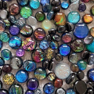 May include: A collection of iridescent glass beads in various shades of blue, green, purple, and black. The beads have a textured, almost metallic finish.