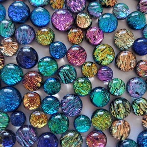 May include: A selection of iridescent glass marbles in various sizes and colours. The marbles display a range of hues, including blue, purple, green, and gold, with a textured, swirling pattern. The marbles are scattered across the surface.