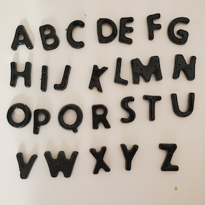 May include: Black plastic letters of the alphabet, A through Z, arranged in three rows on a white background.