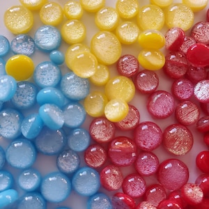 May include: A collection of round, iridescent glass beads in shades of blue, yellow, and red. The beads have a slightly textured surface and are arranged in a random pattern.