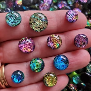 Peut inclure: Une collection de cabochons en verre dichroïque de différentes tailles et couleurs, dont le turquoise, l'or, le rose et le bleu. Les cabochons ont une qualité chatoyante et irisée, reflétant la lumière avec une multitude de teintes. Les cabochons sont ronds et lisses.