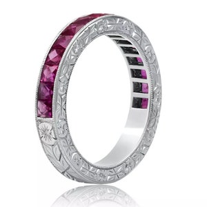 Può includere: Un anello a fascia d'argento con un design inciso floreale e una fila di pietre preziose rubino di forma quadrata.