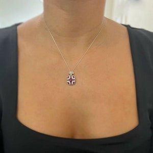 May include: A silver necklace with a red and white pendant. The pendant is shaped like a geometric design with a fan-shaped top.