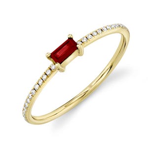 Puede incluir: Un anillo de oro con una sola piedra preciosa roja y una fila de pequeños diamantes alrededor de la banda.