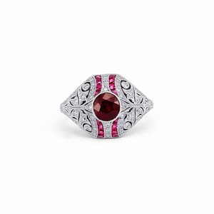 May include: A silver ring featuring a large red gemstone surrounded by smaller white gemstones. The ring has an intricate filigree design.