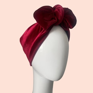 May include: A burgundy velvet headband with a large bow. The headband is worn on a white mannequin head.