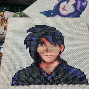 May include: Cross-stitch embroidery of a person with black hair and a blue shirt. The person is looking directly at the viewer.