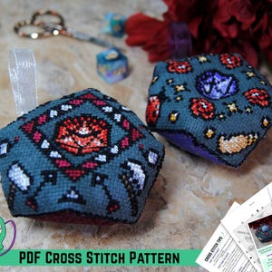 May include: Two cross-stitched dice holders with intricate geometric patterns in teal, red, and white. The text "PDF CROSS STITCH PATTERN" is visible. Other dice and scissors are in the background.