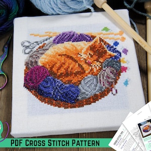 May include: A cross-stitch pattern featuring a ginger cat curled up in a basket of colorful yarn balls. The image is on a white background, with knitting needles, scissors, and a measuring tape nearby. Text at the bottom reads "PDF CROSS STITCH PATTERN."