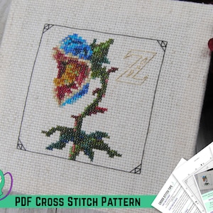 May include: A cross stitch pattern featuring a colorful flower with a blue, red, and yellow center, a green stem, and a gold letter Z in the background. The pattern is titled "Ziku Baba" and is available as a PDF download.