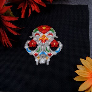May include: A colorful embroidered skull with floral details on a black fabric background. The skull is white with red, green, blue, and yellow accents.