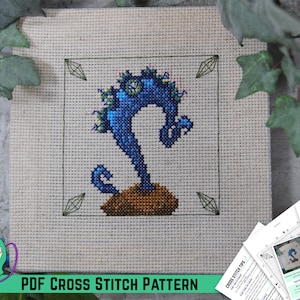 May include: A PDF cross stitch pattern featuring a blue and green plant with a brown base. The pattern is framed by a green border with diamond shapes. The text "PDF CROSS STITCH PATTERN" is at the bottom of the image.