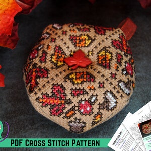 Peut inclure: Un modèle de point de croix pour un coussin rond avec un motif de feuilles d'automne. Le coussin est brun avec des feuilles rouges, orange et jaunes. Le motif est imprimé sur du papier blanc et comprend des instructions de couture.