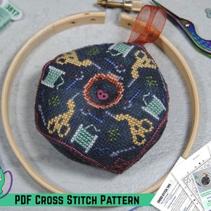 May include: A cross-stitch pattern with a dark blue background and a repeating pattern of scissors, spools of thread, and needles. The pattern is surrounded by a wooden embroidery hoop, with a PDF pattern and scissors in the background. The text "PDF CROSS STITCH PATTERN" is at the bottom.