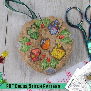 Op de afbeelding: Een voltooid kruissteekpatroon met Pokémon-personages, waaronder Pikachu, Vuurvlieg, Bulbasaur en Squirtle, omringd door hulstbladeren. Het patroon is gestikt op een beige stof en wordt getoond op een houten oppervlak met een schaar, een meetlint en borduurnaalden.