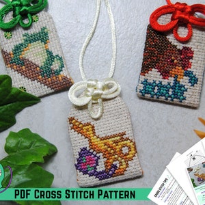 May include: Three cross-stitch pendants featuring a teapot, a bear, and a genie's lamp. Each pendant is on a cream background, with a decorative knot and cord. The text "PDF CROSS STITCH PATTERN" is displayed at the bottom of the image.