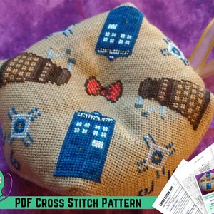 May include: A beige cross stitch ornament featuring a blue TARDIS, a red bow, and brown Daleks. The ornament is attached to a white ribbon and is accompanied by a PDF cross stitch pattern. The pattern includes instructions and a diagram of the ornament.