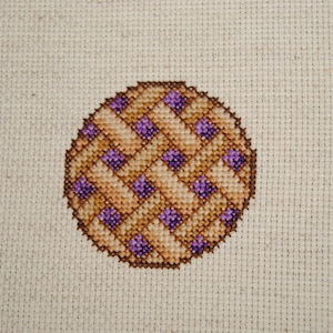 May include: A cross-stitch pattern of a pie with a brown crust and purple filling.