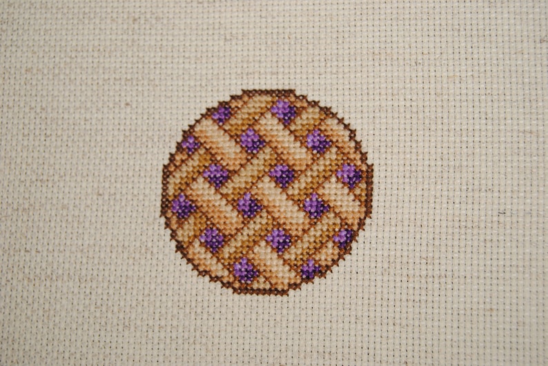 May include: A cross-stitch pattern of a pie with a brown crust and purple filling.
