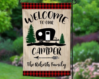 May include: Welcome to our camper garden flag with a red and black buffalo plaid border. The flag features a black silhouette of a camper, trees, and an arrow with the text "Welcome to our camper The Roberts Family".