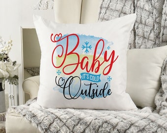 May include: White throw pillow with a blue and yellow watercolor background. The text "Baby It's Cold Outside" is written in red and black cursive lettering.