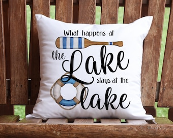 May include: White throw pillow with the text "What happens at the Lake stays at the Lake" in black cursive font. The pillow features a blue and white striped oar and a blue and white life preserver.