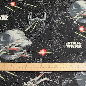 May include: Black fabric featuring a Star Wars design with spaceships, the Death Star, and the Star Wars logo. The design includes X-wing fighters, TIE fighters, and laser blasts against a starry background.