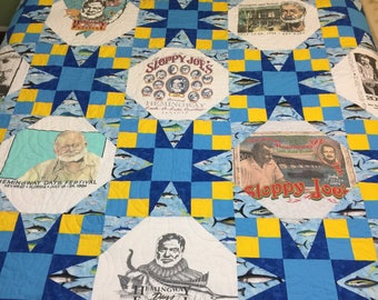 May include: A blue and yellow quilt with a star pattern. The quilt is made from t-shirts with various images and text, including "Sloppy Joe's", "Hemingway Days Festival", and "Key West 1988".