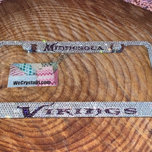 May include: A silver license plate frame with clear rhinestones and the words "Minnesota Vikings" in purple.