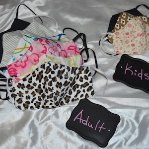 May include: A variety of fabric face masks in different patterns, including leopard print, floral, and stripes. The masks are arranged in two groups, labeled "Kids" and "Adult".