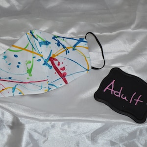 May include: White face mask with a colorful paint splatter design. The mask has black elastic ear loops. A black sign with the word "Adult" written in pink is in the image.