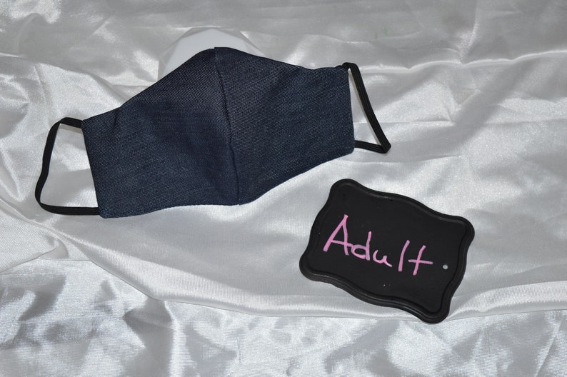 Pu&ograve; includere: Una maschera facciale in denim blu scuro con elastici per le orecchie neri. Uno sfondo nero con la parola "Adulto" scritta con gesso rosa.