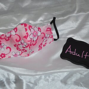 May include: Pink and white floral face mask with black elastic ear loops. The mask is labeled "Adult".