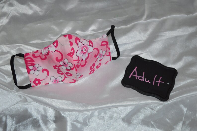 May include: Pink and white floral face mask with black elastic ear loops. The mask is labeled "Adult".