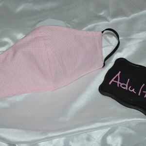 Puede incluir: M&aacute;scara facial de gingham rosa y blanco con el&aacute;sticos de oreja negros. La m&aacute;scara est&aacute; etiquetada como "Adulto".