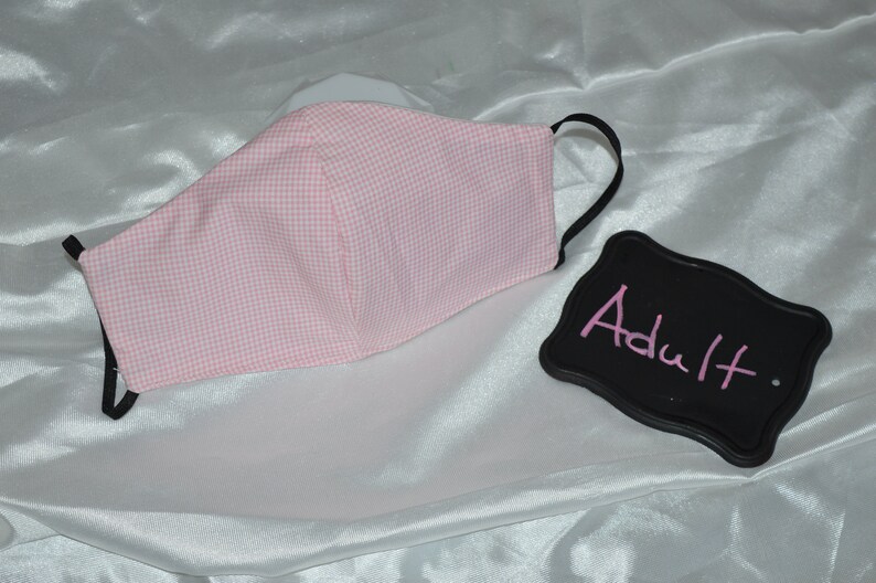 Puede incluir: M&aacute;scara facial de gingham rosa y blanco con el&aacute;sticos de oreja negros. La m&aacute;scara est&aacute; etiquetada como "Adulto".