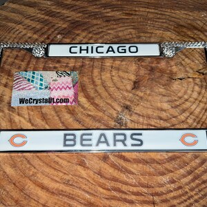 May include: A silver license plate frame with orange rhinestones and the words "CHICAGO BEARS" in white lettering. The frame has a clear plastic insert for a license plate.